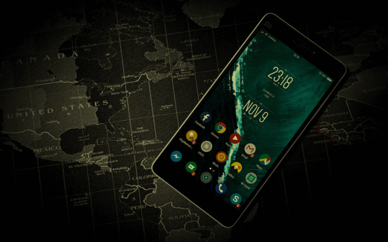 The photograph depicts a smartphone with a date display and app icons, set against a dark world map, implying the blending of digital and geographic information.