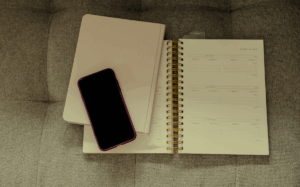 A smartphone placed next to a notebook and planner, suggesting the use of digital and analog tools for organization and productivity.