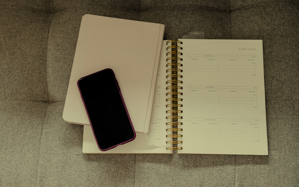 A smartphone placed next to a notebook and planner, suggesting the use of digital and analog tools for organization and productivity.