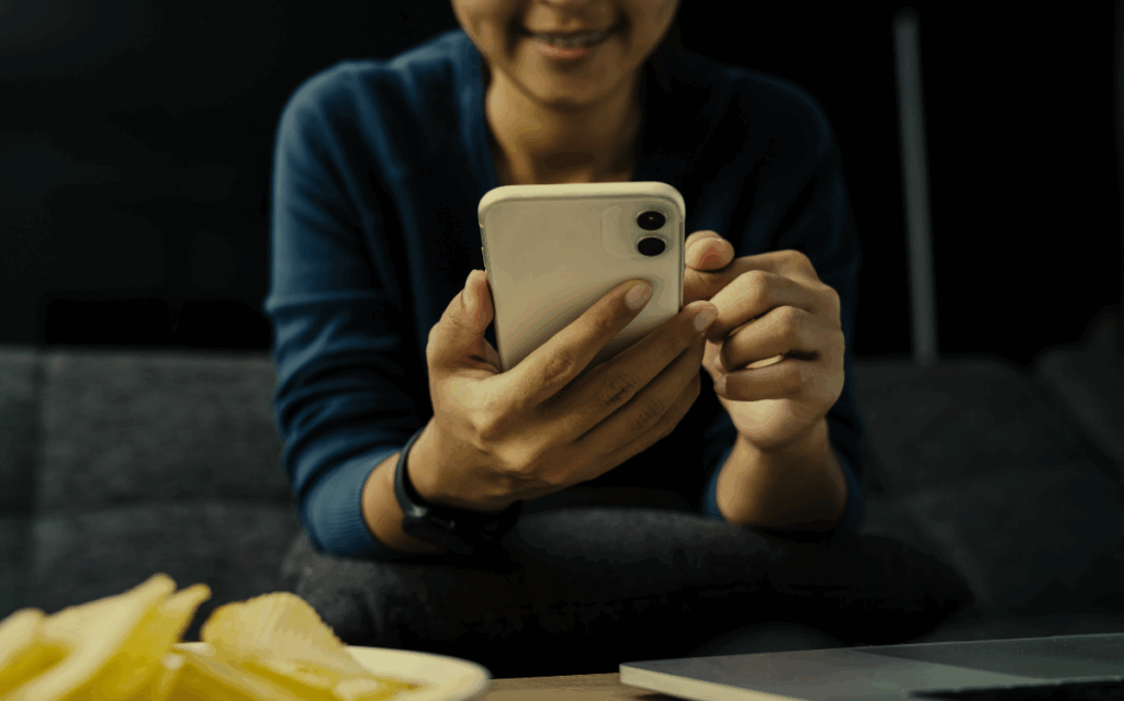 A person smiling while intently using a mobile phone, suggesting the integration of technology in daily life and personal interactions.