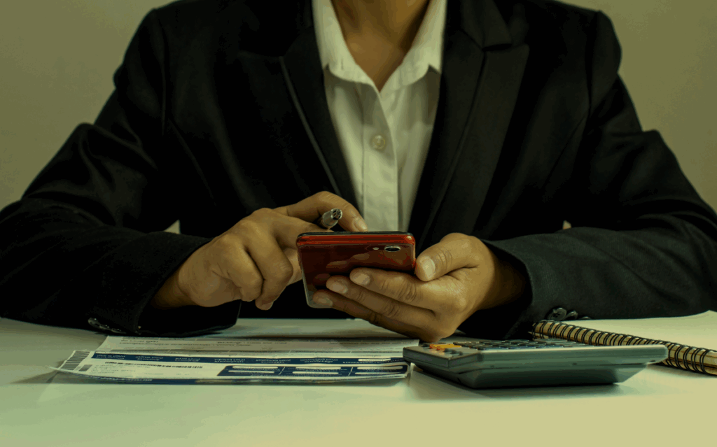 A person's hands holding a smartphone while using a calculator, suggesting the need for financial management and digital tools.