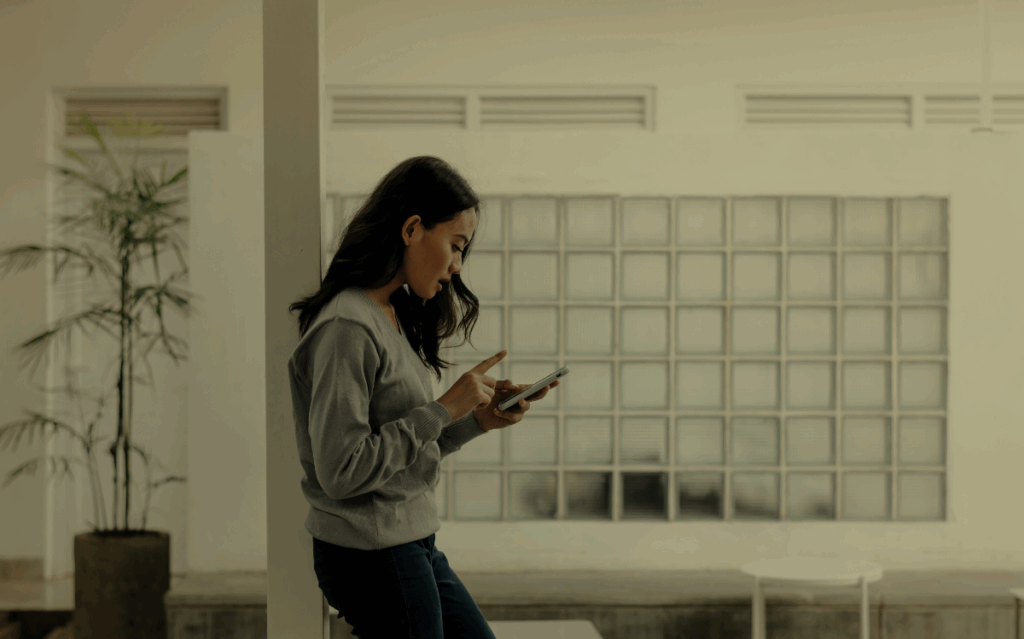 A person standing in an indoor setting, intently focused on using a mobile device, suggesting the integration of technology in daily life.