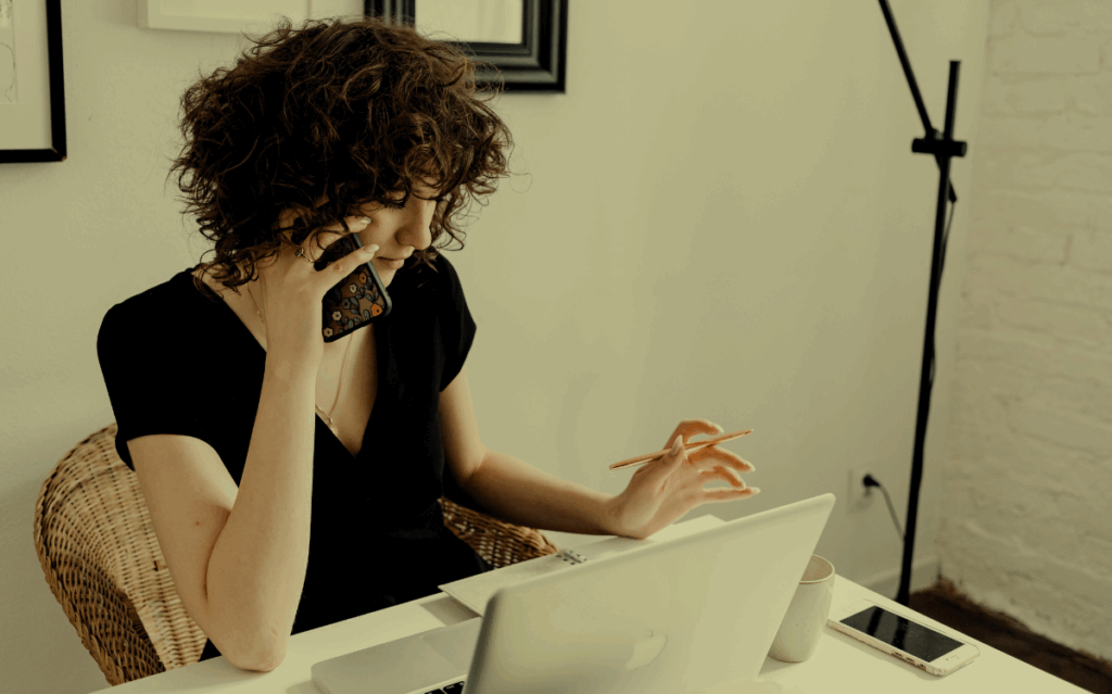 A person with curly hair using a laptop and speaking on a mobile device, suggesting the integration of technology in work or creative pursuits.