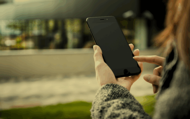 Hands are shown holding a mobile device, with a blurred natural setting visible in the background, implying the ubiquity of smartphones in modern environments.