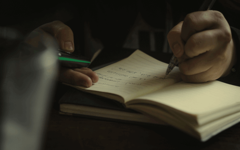 Hands holding a pen and writing in an open notebook, suggesting the value of traditional methods for documentation and learning.