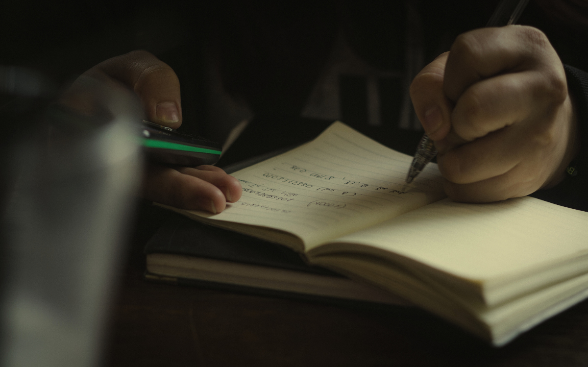Hands holding a pen and writing in an open notebook, suggesting the value of traditional methods for documentation and learning.